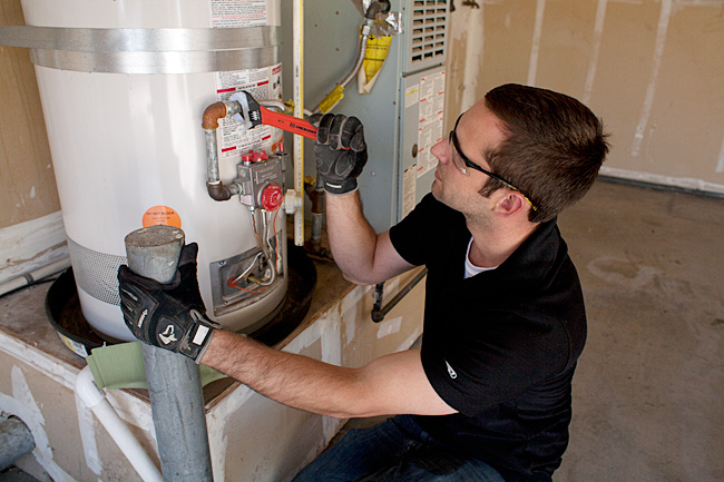 plumber in Tacoma repairs an American Standard water heater in a garage